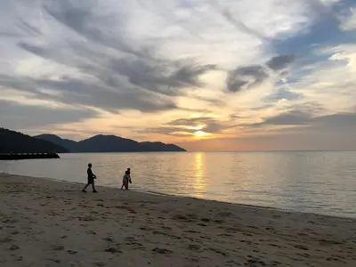 two people walking on the beach at sunset at By The Sea Luxury Beachfront Resort 223 in Batu Ferringhi