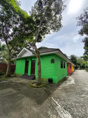 a green building with a tree next to a street at Hotel O Rumah Rehat Awana in Kampong Nanas