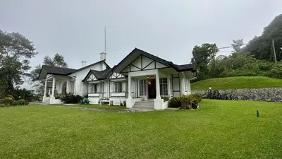 a white house with a grass yard at Bukit Ruil Bungalow - Clementine Suite in Tanah Rata