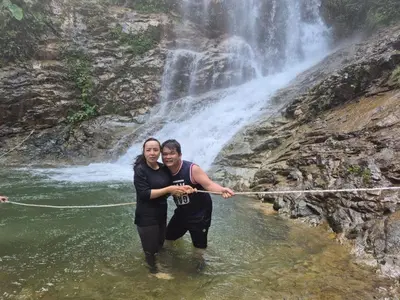 a man and woman standing in the water in front of a waterfall at Sunny Lake House - Entire bungalow, 5 rooms, 16 persons in Behrang Hulu