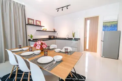 a dining room table with white chairs and a kitchen at Solok Sungai Emas By Plush in Batu Ferringhi