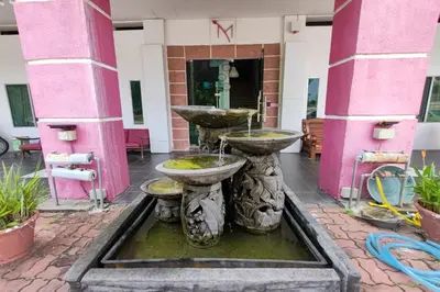 a fountain in front of a building with pink columns at Maleeq Hotel Meru Ipoh in Ipoh