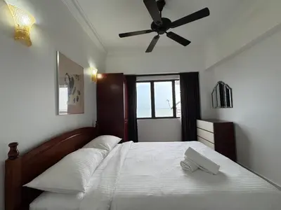 a bedroom with a bed with white sheets and a ceiling fan at Seaview - Sri Sayang in Batu Ferringhi