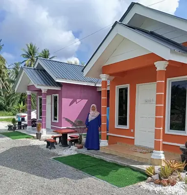 a woman standing in front of a pink house at D'SQ Homestay in Tanjung Karang