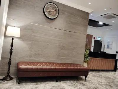a brown leather couch against a wall with a clock at De Quinton Hotel in Ipoh