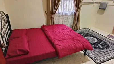 a bed with a red comforter in front of a window at Homestay Kak Rose Kuala Lipis in Kuala Lipis