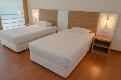 two beds in a hotel room with white sheets at The CEO Executive Suites in Bayan Lepas