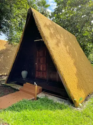 a small house with a thatch roof on the grass at Kuala Woh Resort in Tapah