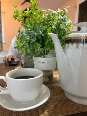a cup of coffee and a vase with flowers on a table at RumaTisa in Teluk Intan