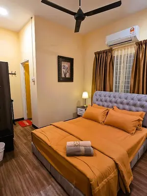 a bedroom with a large bed with orange sheets and a fan at Homestay Desa Kati Kuala Kangsar in Kuala Kangsar