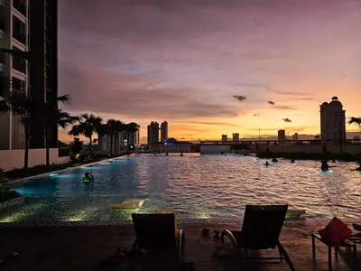 a swimming pool with chairs in the water at sunset at New Metropol 3 Bedrooms Pool View in Bukit Mertajam