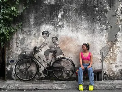 a woman sitting on a bench in front of a wall with a bike at Georgetown Homestay in George Town
