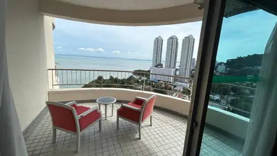 a balcony with two chairs and a table and a view of the ocean at Maisie Rainbow Penang in Tanjung Bungah