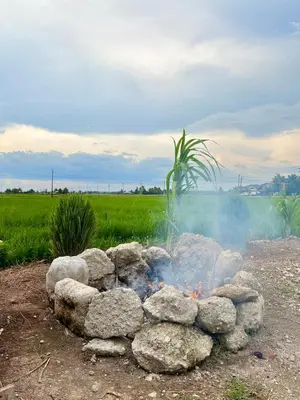 a fire pit with rocks in front of a field at Rumah Teduh in Gua Sai