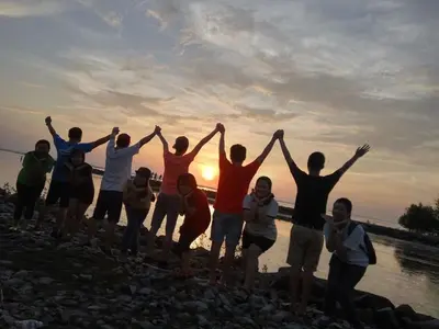 a group of people standing on a beach with their hands up at Quadruple Traditional Wooden GuestHouse in Balik Pulau