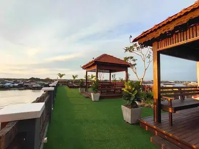 a resort with a green lawn and benches on the water at Capital O 91170 Kurau Bay Hotel in Kuala Kurau