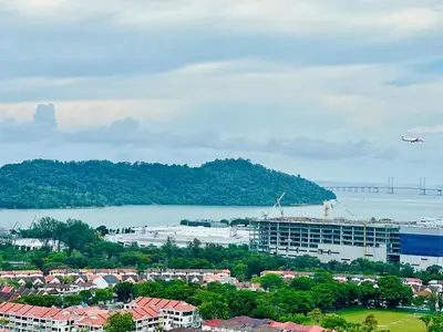 an airplane is flying over a city with a body of water at Sea Bridge View Sky Pool Cozy 3BR Retreat airport 9pax in Bayan Lepas