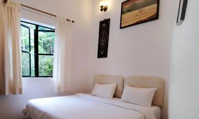 a bedroom with a bed with white sheets and a window at Holiday Bungalow Guesthouse in Tanah Rata