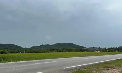 an empty road with a field and mountains in the background at Homestay Teluk Bayu in Sungai Petani