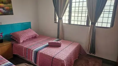 a bedroom with a bed with a pink blanket and two windows at Rumah Inap Haziq in Seri Manjung
