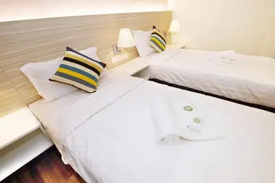 two beds in a hotel room with white sheets and pillows at Good Luck Inn in Ayer Itam