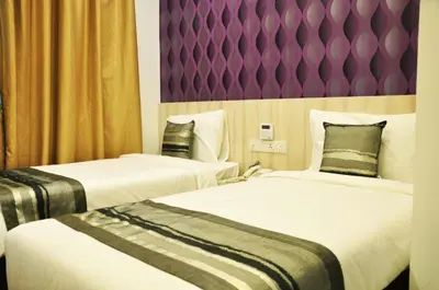 two beds in a hotel room with a purple wall at Valya Hotel, Ipoh in Ipoh