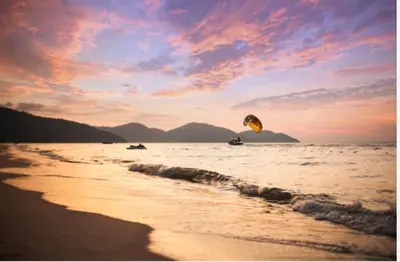 a person is flying a kite on the beach at By the sea Beach Front, Seaview And Pool side in Batu Ferringhi