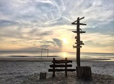 a wooden sign on a beach with the sunset at Homestay Selesa KPP Guest House in Gua Sai