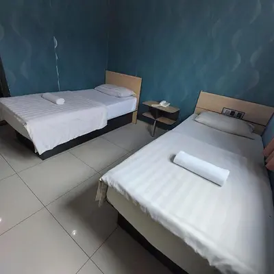 two beds in a small room with two tables at Sam Hotel Sitiawan in Sitiawan