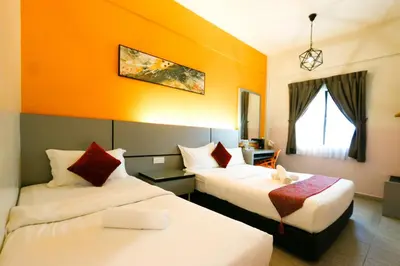 two beds in a hotel room with an orange wall at Travelland Hotel in Ipoh