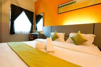 a bedroom with a large white bed with an orange wall at Travelland Hotel in Ipoh