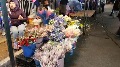 a woman sitting next to a display of flowers in buckets at Famous night market Cameron Highlands Nearby in Cameron Highlands