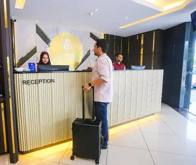 a man standing at a reception counter with a suitcase at Golden Nasmir Hotel in Bukit Mertajam