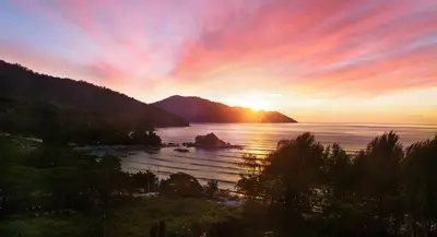 a sunset over a body of water with a mountain at The Bayview Beach Resort in Batu Ferringhi