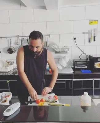 a man standing in a kitchen preparing food on a cutting board at Beds In Garden Hostel in Ipoh