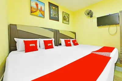a bedroom with two beds with red pillows and a tv at Hotel O Bamboo Inn in Batu Ferringhi