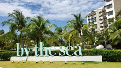 a sign that says by the sea in front of palm trees at By The Sea Beach Luxury Resort - Batu Ferringhi in Batu Ferringhi