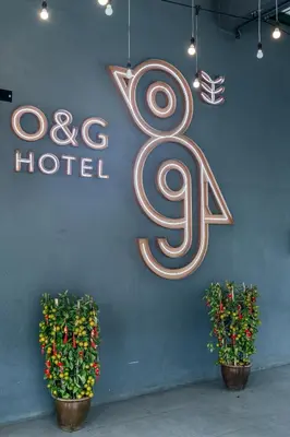 a hotel sign hanging on a wall with two plants at O&G Hotel Parit Buntar in Parit Buntar