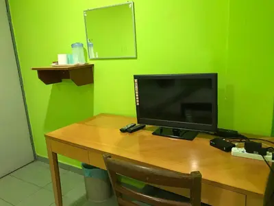 a computer monitor on a wooden desk with a green wall at Hotel Cahaya in Tanjung Malim