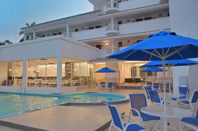 a pool with tables and chairs and blue umbrellas at AVI Pangkor Beach Resort in Pangkor
