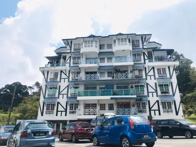 a large white building with cars parked in front of it at MERLIN HOME DESA ANTHURIUM in Tanah Rata