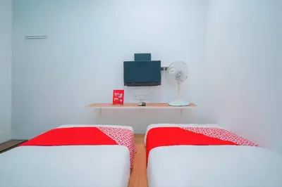 a room with two beds and a tv and a desk at Hotel O V Stay Guesthouse in Ayer Itam