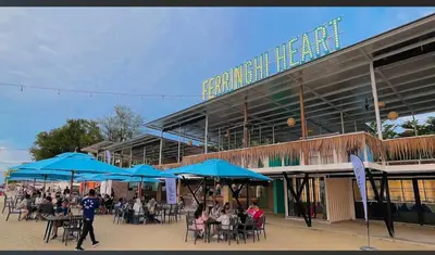a group of people sitting at tables under blue umbrellas at PoolView Resort Batu Ferringhi 502 - 2 Rooms in Batu Ferringhi