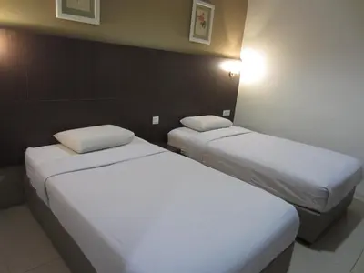 two beds in a hotel room with white sheets at Radiant Hotel in Sitiawan