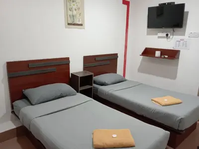 two beds in a room with a tv on the wall at Evonne Budget Hotel in Tanah Rata