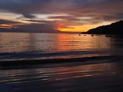a sunset on the beach with boats in the water at KAMILA MOTEL TELUK SENANGIN in Lumut