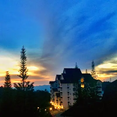 a building with lights on in front of a sunset at The Antler Silverpark Fraser's Hill in Bukit Fraser